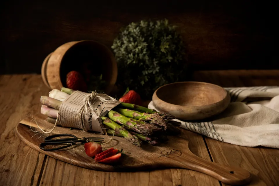 Asparagus tied with string and halved strawberries on a wooden board