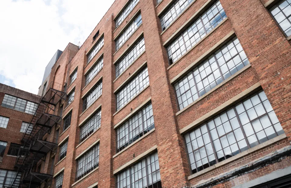 The brick facade of an apartment building with rows of tall windows and a fire escape