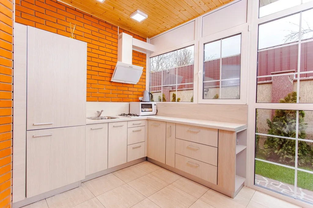 A compact kitchen with pale units and a worktop, with windows looking onto a garden