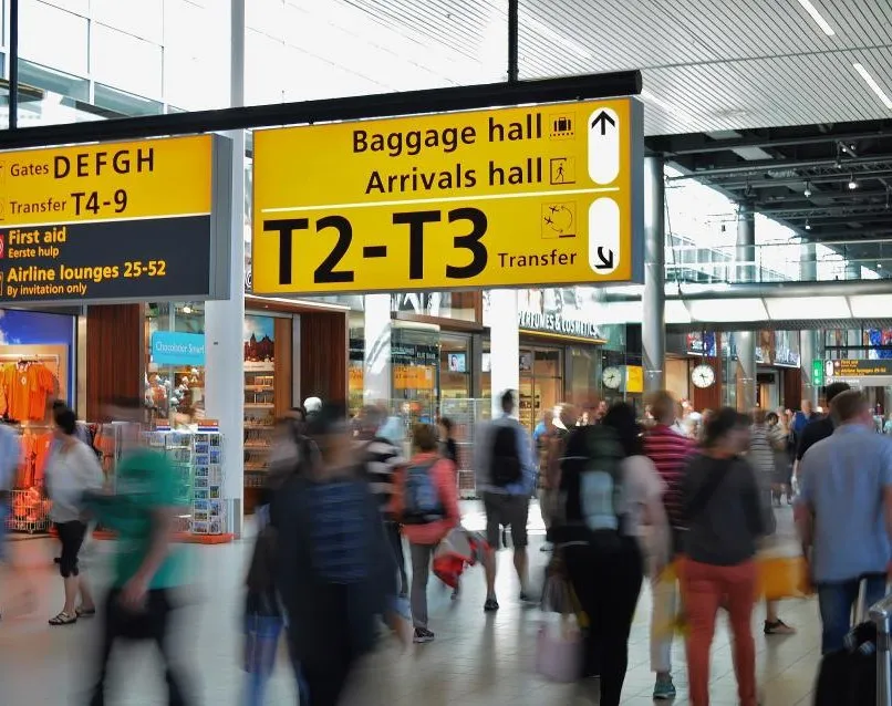 Travellers crossing an airport concourse beneath large yellow signs for the baggage and arrivals halls